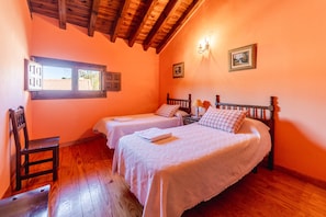 Quarto com duas camas, piso de madeira, janela com persianas e teto de madeira.