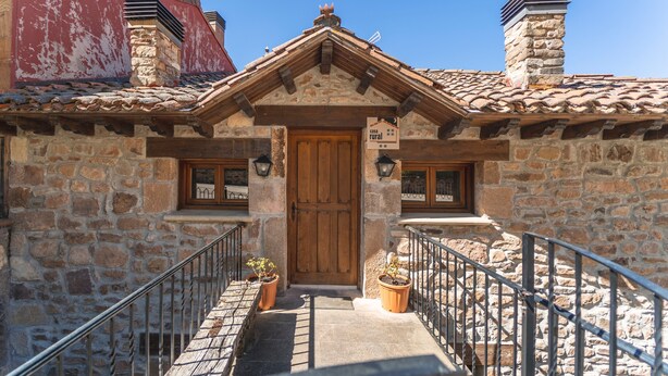 Un edificio de piedra con puerta de madera, una escalera y dos macetas.