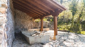 Una estructura de paredes de piedra con una pérgola de madera, escalones de piedra y suelo de piedra.