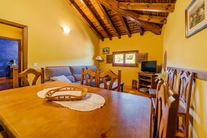 Uma sala de jantar com mesa de madeira, cadeiras, televisão e uma janela com persianas.