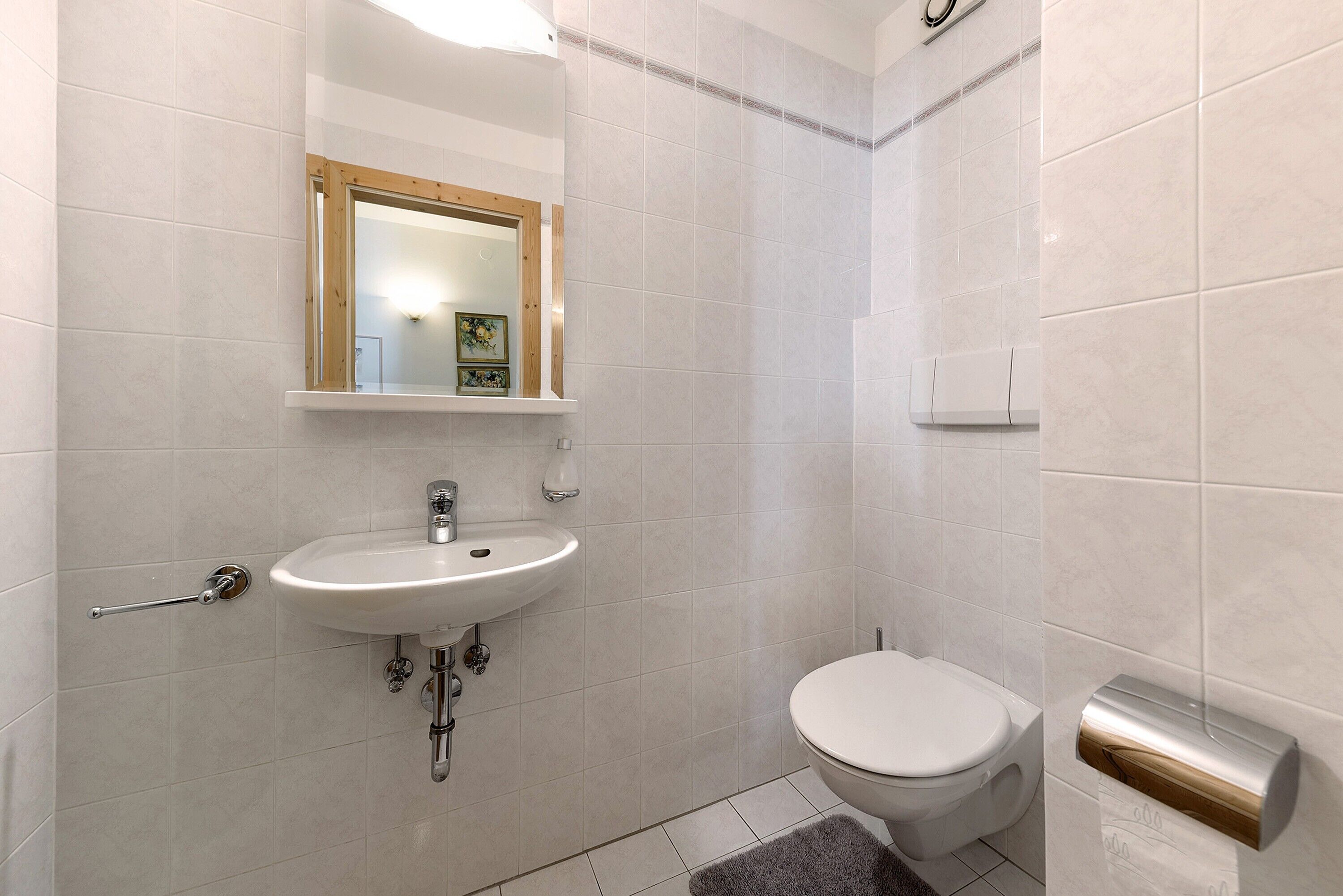 A bathroom with a sink, toilet, mirror, and towel dispenser.