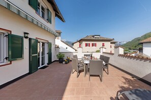 A patio with outdoor furniture, a table, and chairs, a building with green shutters, and a mountain in the background. - Apartment 'Kreutnerbinderhof' with Mountain View, Private Terrace and Wi-Fi (Terlano)