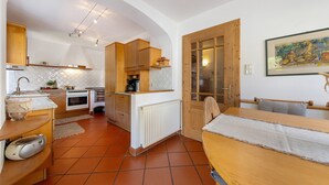 A compact kitchen with wooden cabinets, a white countertop, and a dining area with a table and bench. - Apartment 'Kreutnerbinderhof' with Mountain View, Private Terrace and Wi-Fi (Terlano)