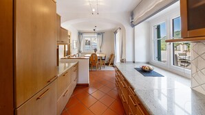 A kitchen with wooden cabinets, a tiled floor, a countertop, and a view through large windows. - Apartment 'Kreutnerbinderhof' with Mountain View, Private Terrace and Wi-Fi (Terlano)