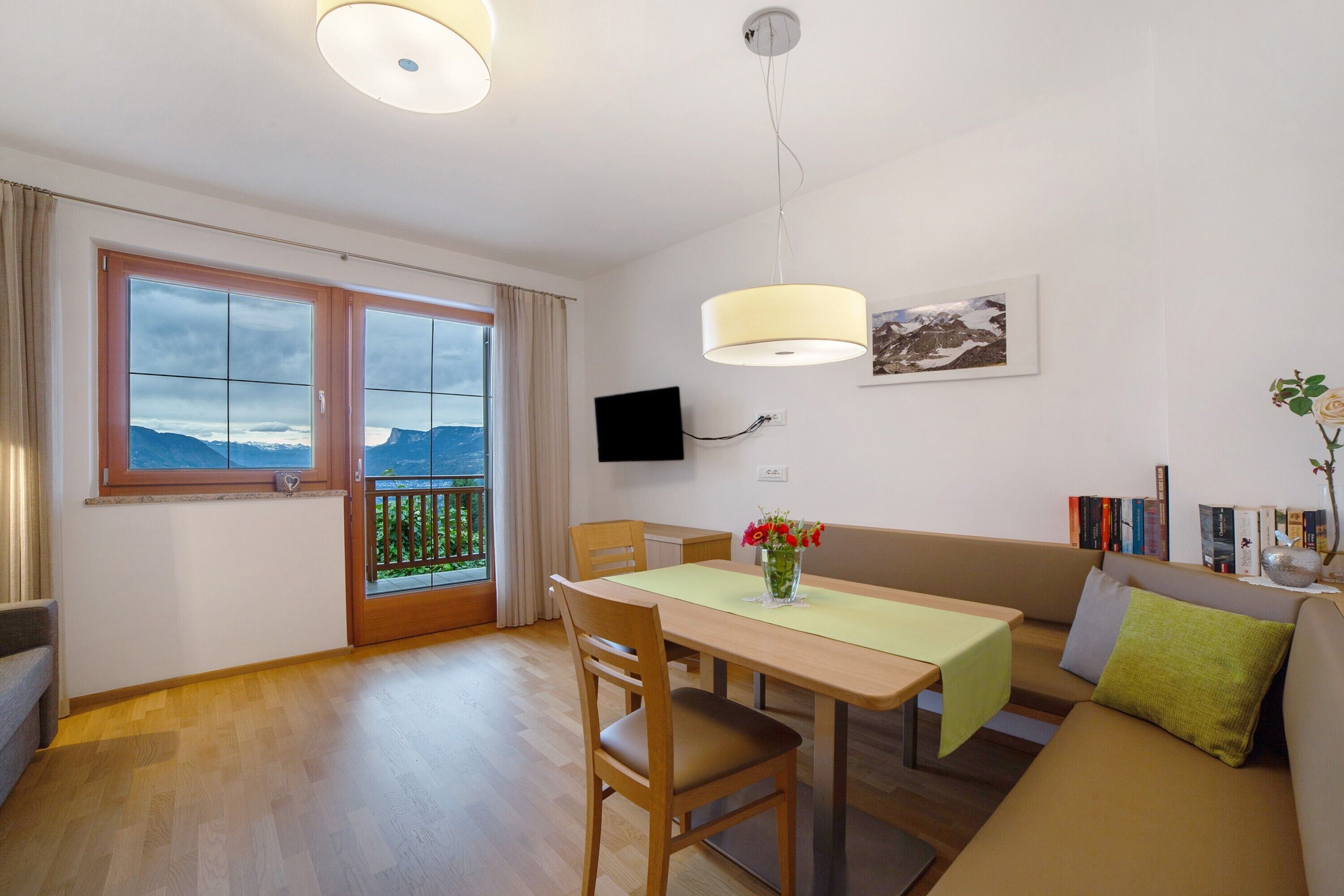 Une chambre moderne équipée d’une table à manger, de chaises, d’un canapé, d’une télévision et d’une fenêtre donnant sur les montagnes.