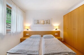 A room with two beds, a wooden wardrobe, a painting on the wall, and two bedside lamps.