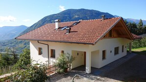 A two-story house with a red-tiled roof, white walls, and a view of mountains. - Apartment 'Oberötzbauer  Alpenrose' with Mountain View, Shared Garden and Wi-Fi (Tirol)