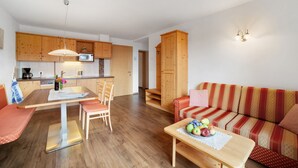 Een moderne keuken met houten kastjes, een eettafel met stoelen en een bank met een decoratieve hoes.