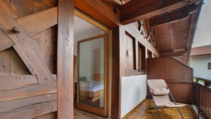 Een houten balkon met een schuifdeur van glas, een houten leuning en een enkele beigekleurige stoel.