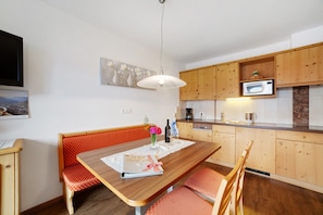 A dining area with a wooden table, bench, and chairs, a kitchen with wooden cabinets, and a hanging light fixture.