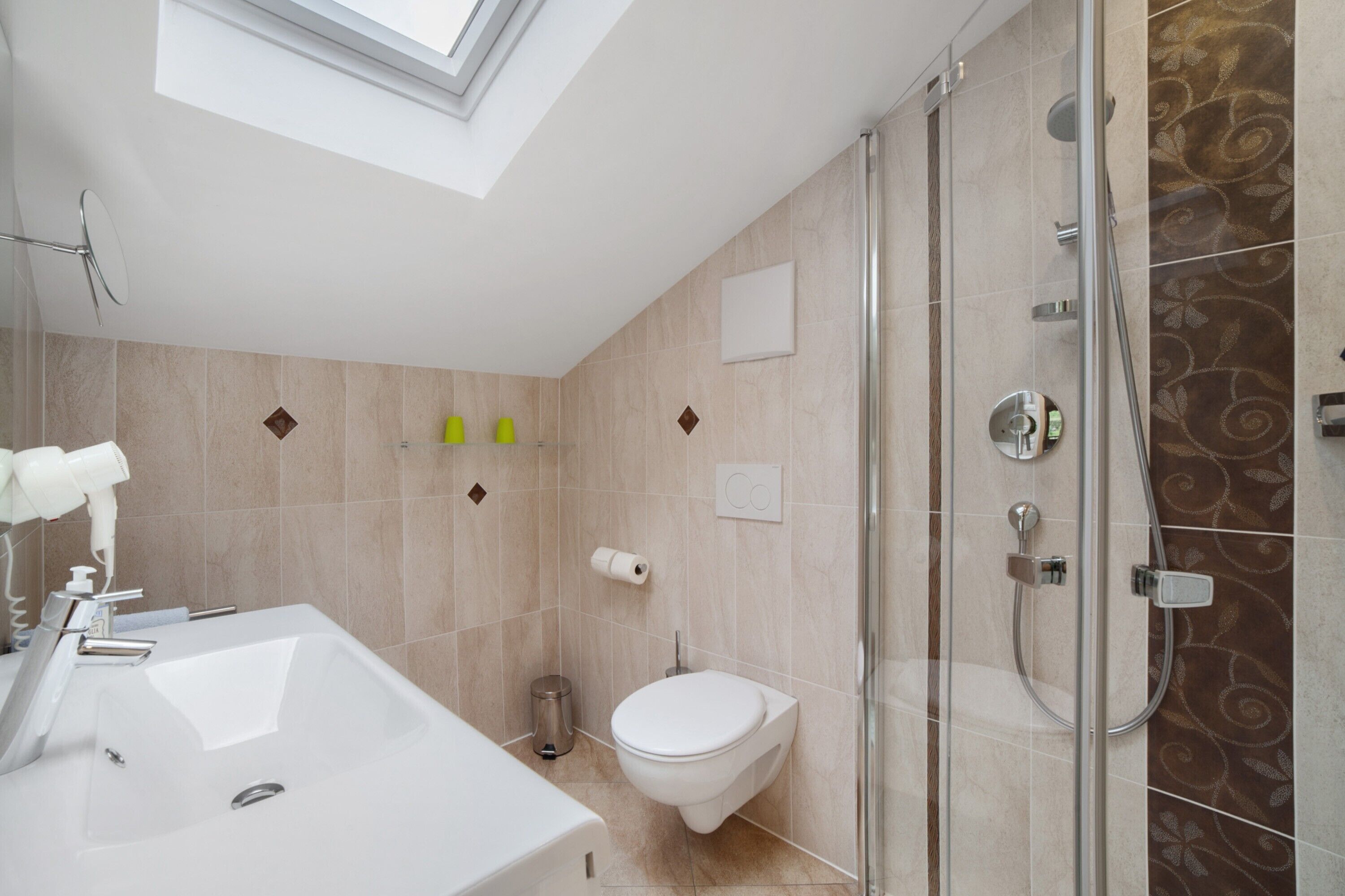 A modern bathroom with a skylight, a shower, a sink, and a toilet.