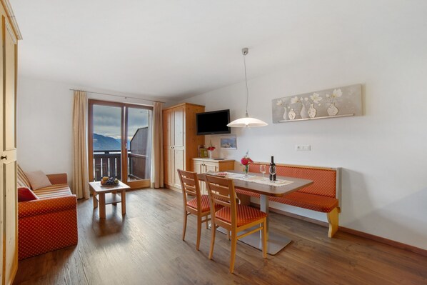 A room with a dining table, chairs, a bench, a TV, a window with a view, and a painting on the wall.