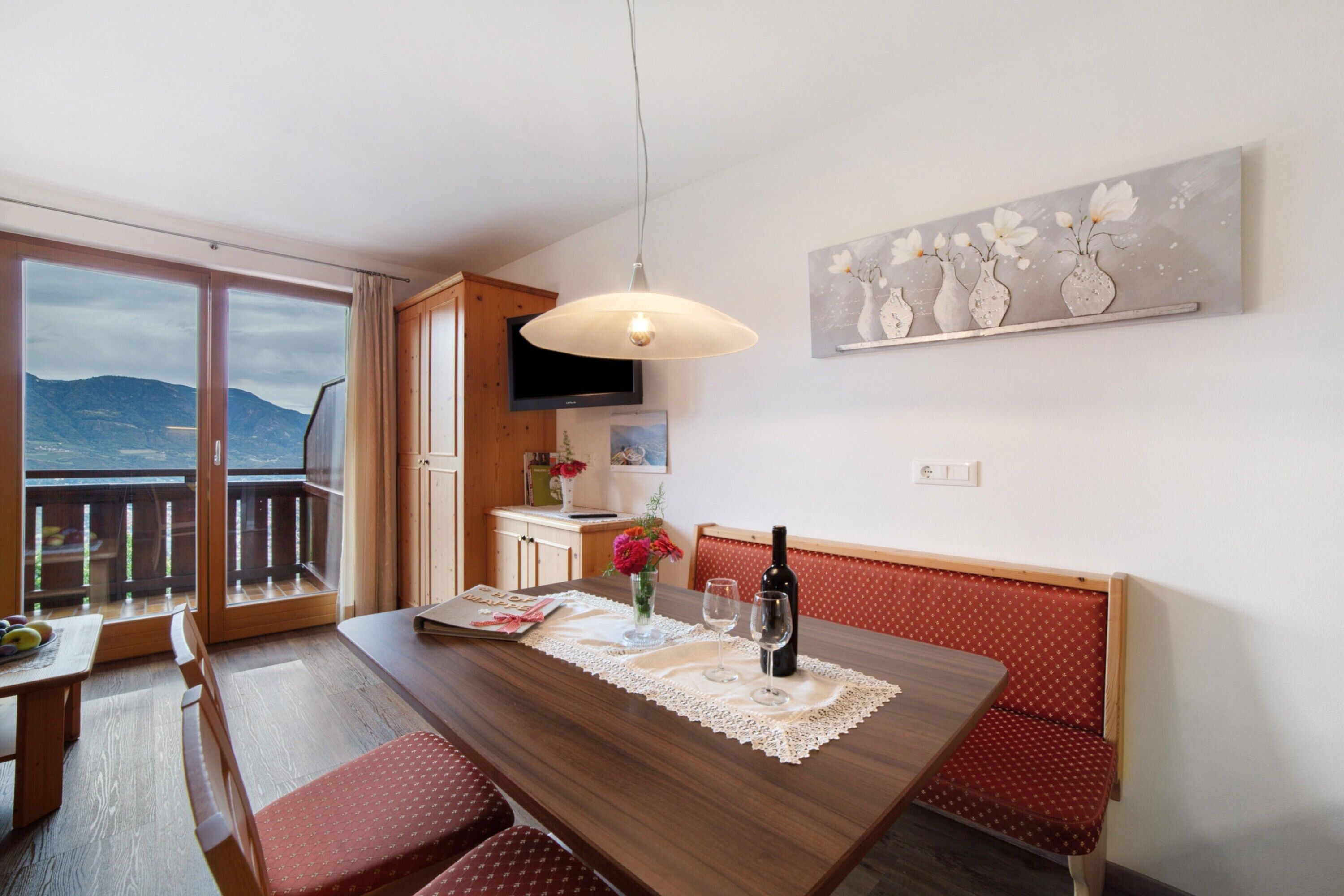 A dining area with a wooden table, bench seating, a bottle of wine, and a view through a glass door.