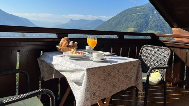 A table with breakfast items and a glass of orange juice on a balcony with a mountain view. - Apartment 'Oberötzbauer  Edelweiss' with Mountain View, Shared Garden and Wi-Fi (Tirol)
