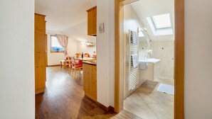 A room with a wooden floor, a dining area with a table and chairs, a kitchen area, and a bathroom with a skylight. - Apartment 'Oberötzbauer  Edelweiss' with Mountain View, Shared Garden and Wi-Fi (Tirol)