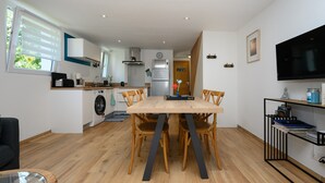 A modern kitchen with a dining area, a TV, and a bookshelf. - Holiday Home 'La Fleur De Vie' with Private Garden and Wi-Fi (Pluneret)