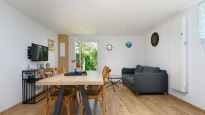 A modern living space with a dining table, chairs, a sofa, a TV, and a door leading to a garden. - Holiday Home 'La Fleur De Vie' with Private Garden and Wi-Fi (Pluneret)