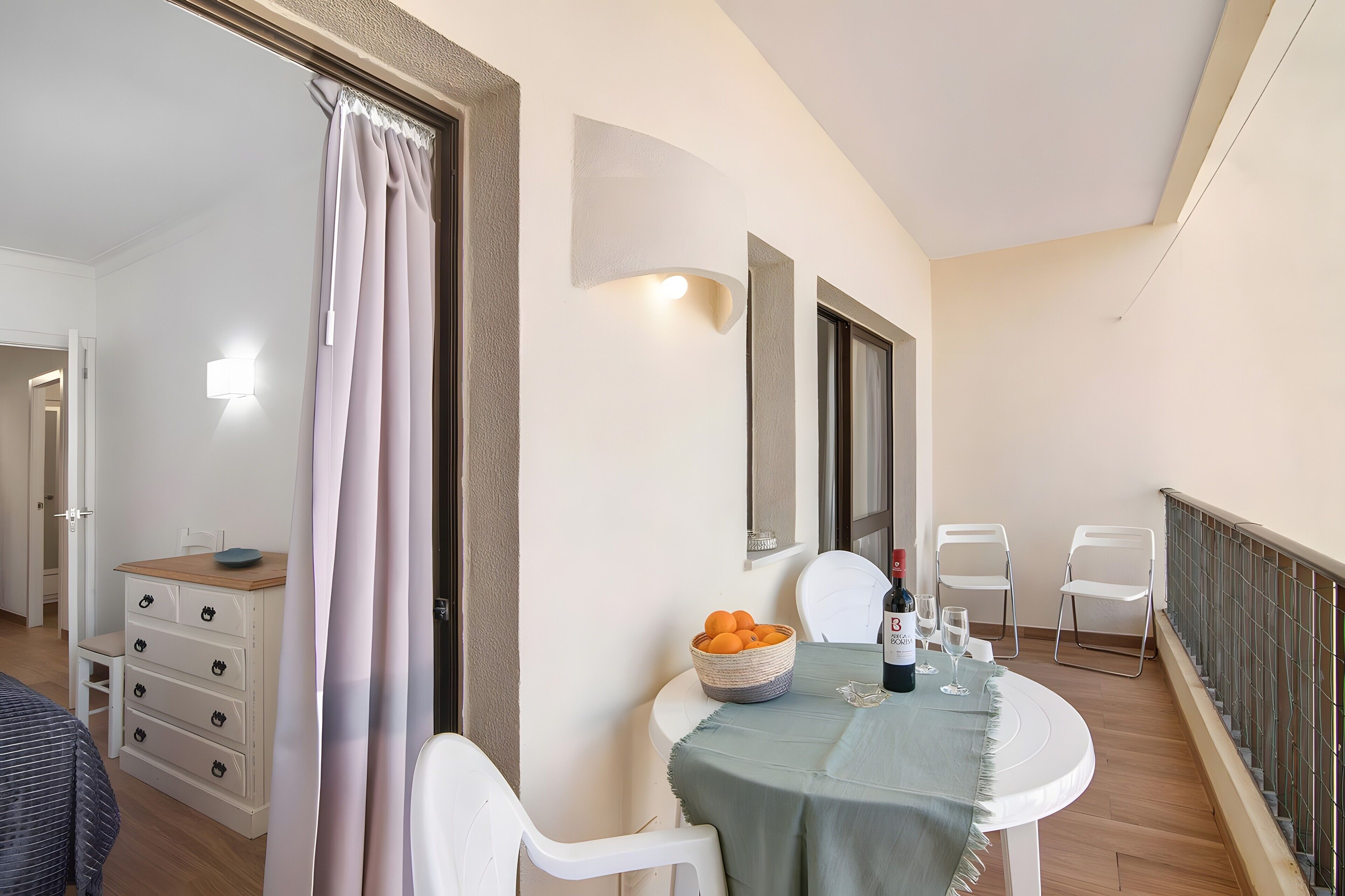 Un balcon avec une table, des chaises, un panier d’oranges et une bouteille de vin.