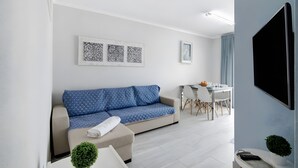 A modern living room with a sofa, a dining table, and a flat-screen TV. - Apartment 'Seaside  - Praia Da Rocha' with Mountain View, Shared Pool and Wi-Fi (Portimão)