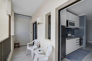 A balcony with white plastic chairs, a small table, and a bottle of wine.