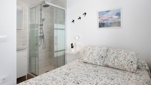 A bedroom with a bed, a nightstand, a wall-mounted picture, and a glass-enclosed shower. - Studio Apartment 'Atico Juani' with Private Terrace, Wi-Fi and Air Conditioning (Conil de la Frontera)