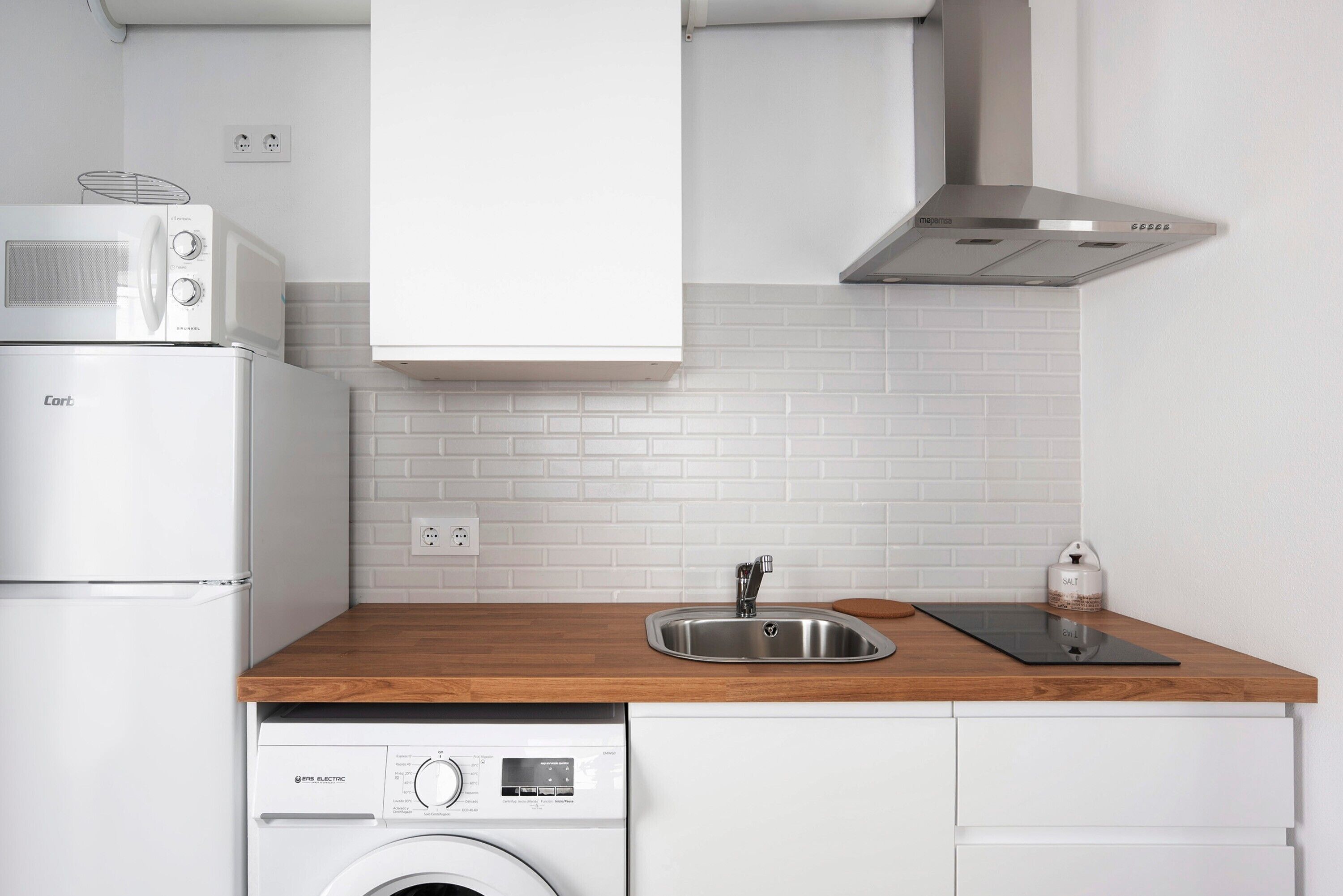 A kitchen with a washing machine, a microwave, a sink, and a stainless steel range hood.
