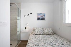 Une chambre à coucher avec un lit, une douche, un tableau accroché au mur et une petite étagère avec une plante.