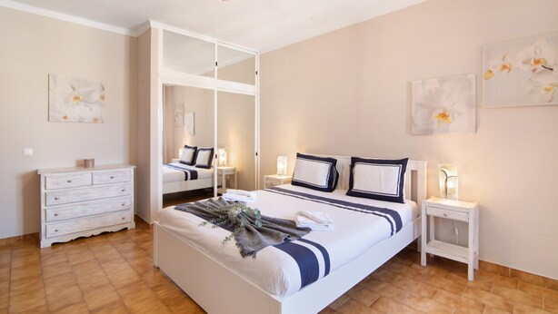 A bedroom with a bed, bedside tables, a dresser, and artwork on the walls.