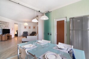 A dining area with a table set for four, a television in the background, and a refrigerator to the right.