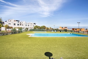 A swimming pool surrounded by a well-maintained lawn, with a multi-story building in the background.