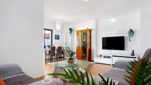 Un salon moderne avec une table basse en verre, un téléviseur à écran plat et un coin repas à l’arrière-plan.