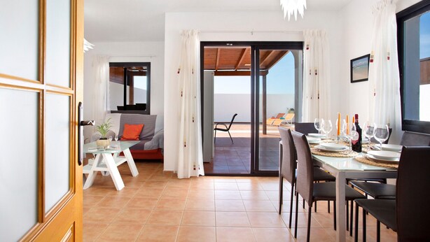 Un coin repas avec une table dressée pour quatre personnes, un canapé et une vue à travers une porte vitrée.