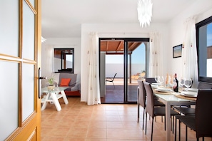 A dining area with a table set for four, a sofa, and a view through a glass door.