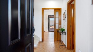 Un couloir avec une porte noire, une porte en bois et un sol carrelé.
