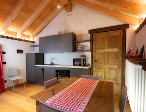A compact kitchen with modern appliances, a dining table with a checkered tablecloth, and a wooden door.