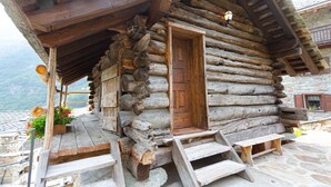 Une cabane rustique en rondins de bois, avec une porte en bois, un petit porche avec des marches et un mur de pierres en arrière-plan.