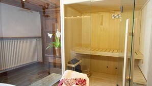 Un sauna doté d’une paroi en verre, d’un banc en bois, d’une serviette et d’une plante en pot.