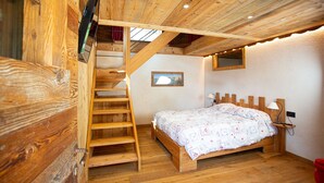 Un intérieur en bois comprenant un lit, un escalier en bois, un téléviseur et une petite fenêtre.