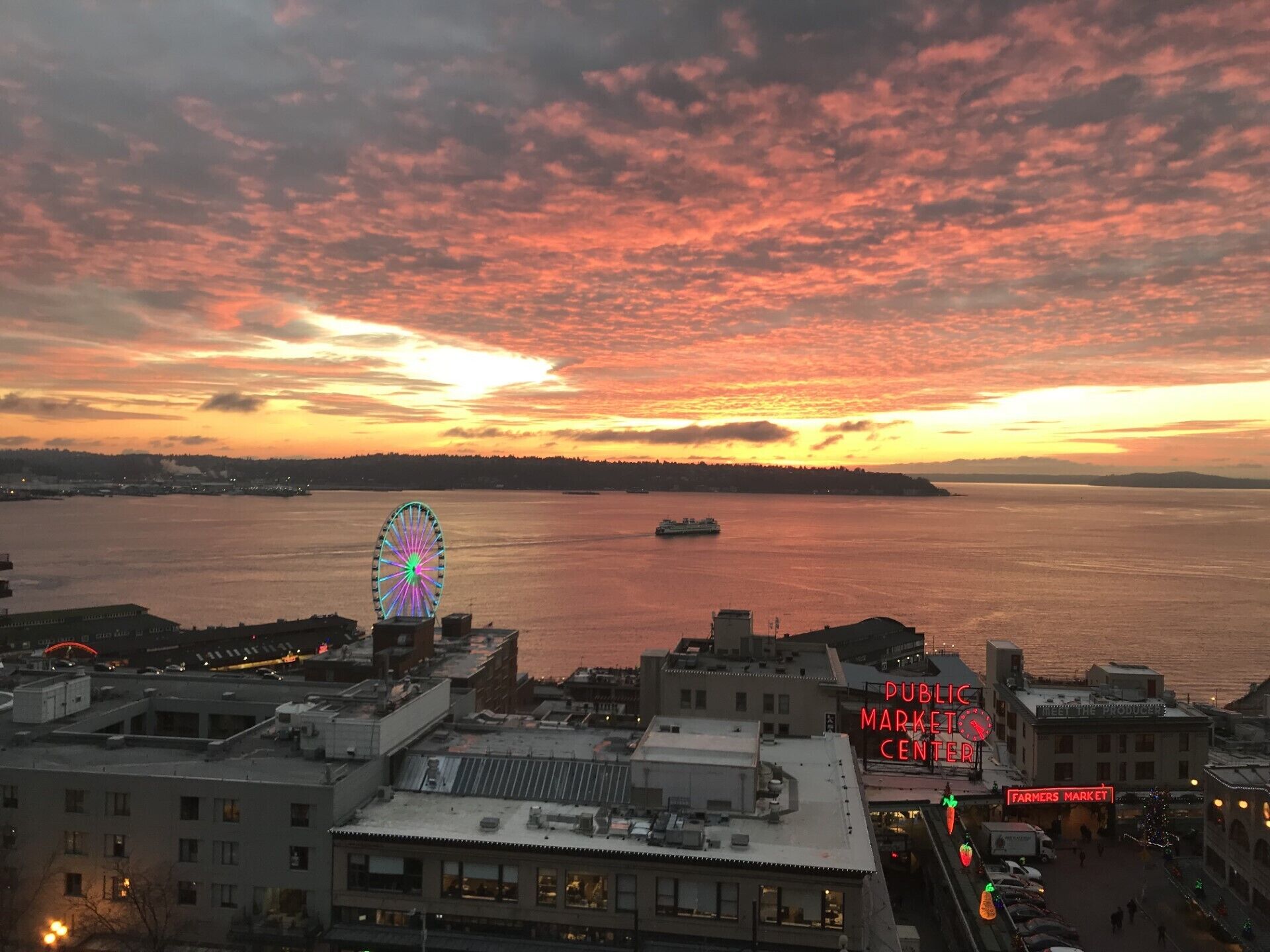 Une vue sur le coucher de soleil au-dessus d’une promenade en bord de mer, avec une grande roue et un marché public.