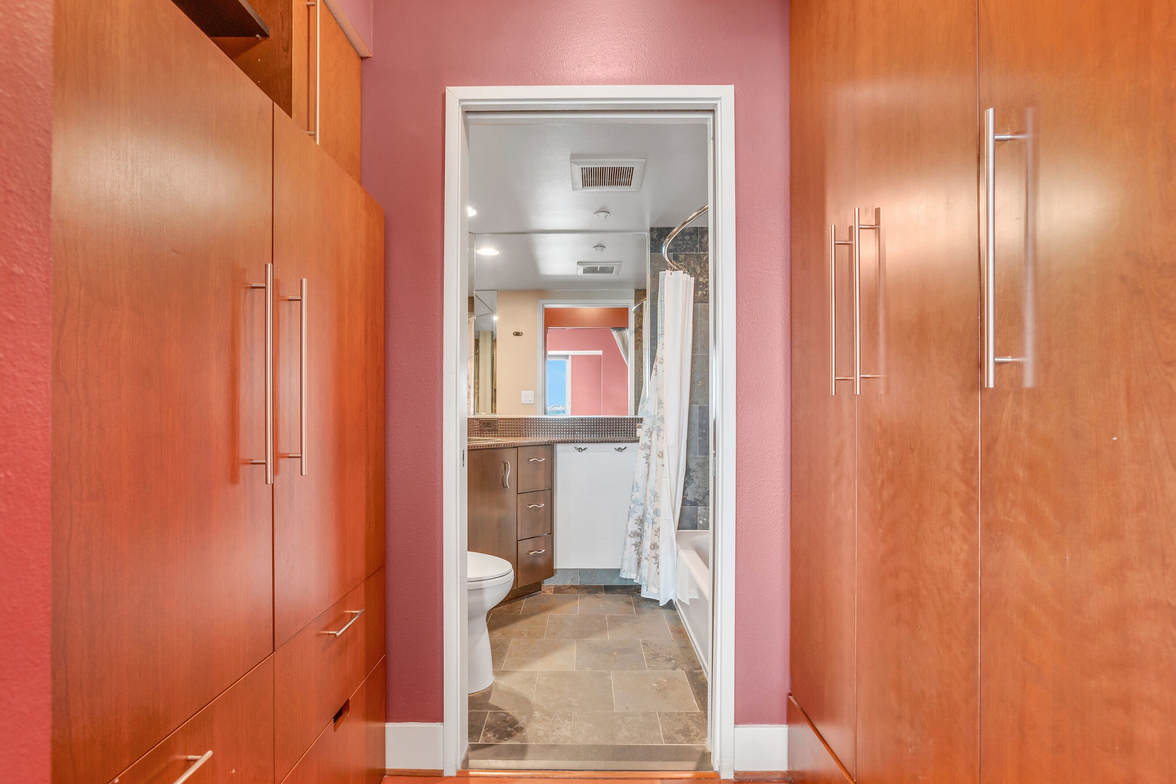 A narrow hallway with wooden cabinets and a bathroom visible through an open door.