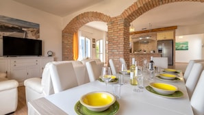 A dining area with a brick archway, white furniture, and a kitchen in the background. - 'Villa Sara' with Private Pool, Wi-Fi and Air Conditioning (Sorso)