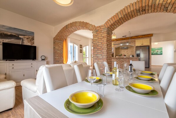 A dining area with a brick archway, white furniture, and a kitchen in the background.