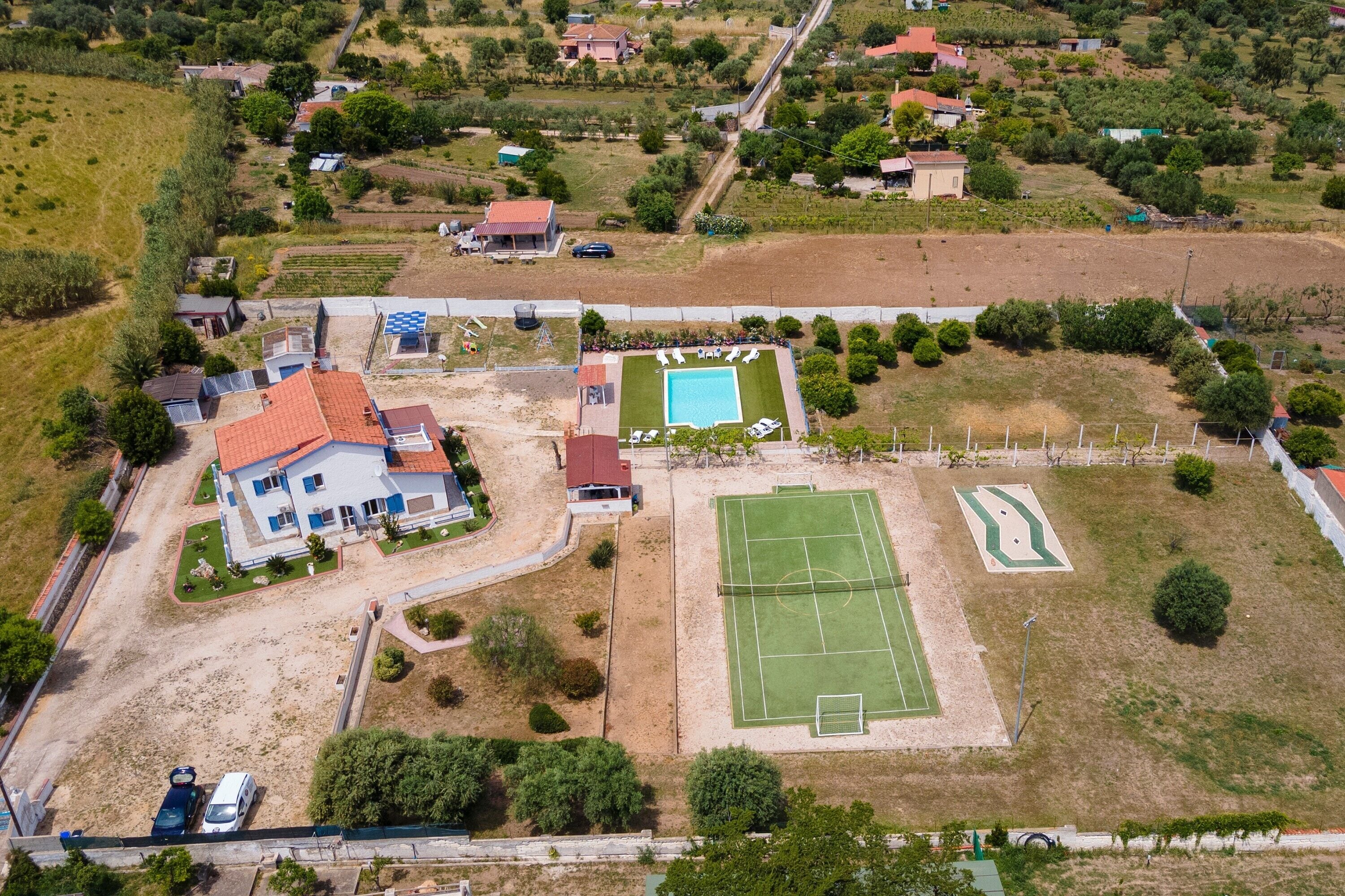 An aerial view of a residential area with a house, a swimming pool, and a tennis court.