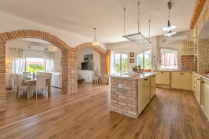 A spacious kitchen with brick arches, wooden flooring, and a dining area with white chairs.