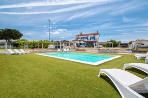 A swimming pool with white lounge chairs, a house with a red roof, and a clear sky.