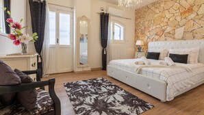 A bedroom with a large bed, a chandelier, a stone wall, a mirror, and a window. - 'Villa Sara' with Private Pool, Wi-Fi and Air Conditioning (Sorso)