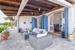 A covered outdoor seating area with wicker furniture, a stone floor, and a view of the interior.
