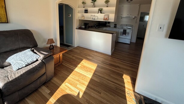 A modern living room with a sofa, a coffee table, and a kitchen area with a stove and cabinets.
