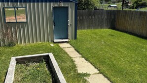 A backyard with a metal shed, a wooden deck, and a concrete path.