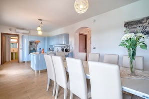 A modern kitchen with blue cabinets, a central island, and a dining area with white chairs and a table. - Villa Della Felicità with Private Pool, Wi-Fi and Air Conditioning (Sorso)